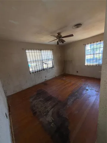 an empty room with wooden floor fan and windows
