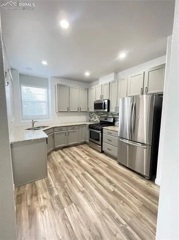 a large kitchen with a refrigerator a sink dishwasher a stove and white cabinets with wooden floor