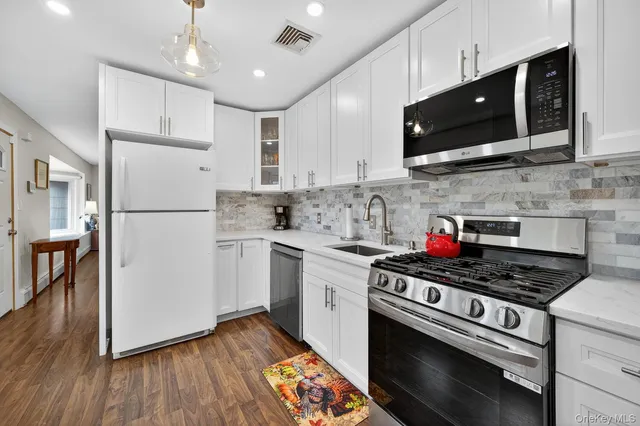 a kitchen with stainless steel appliances granite countertop a stove top oven a refrigerator a sink and dishwasher with wooden floor