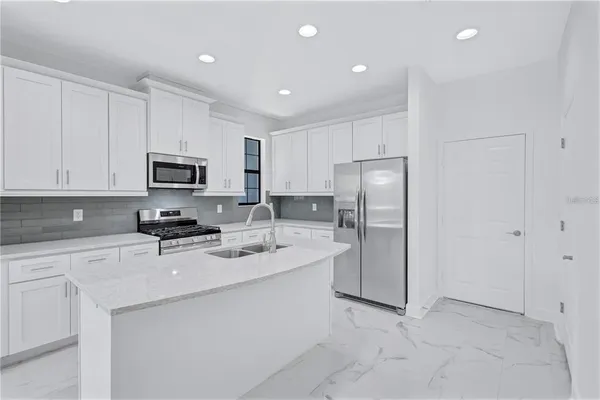 a kitchen with stainless steel appliances granite countertop a refrigerator a stove a sink a microwave and white cabinets