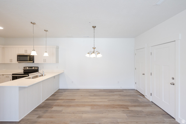 675 West 4500th South, Unit P204 Mapleton, UT 84664 - Photo 13 of 16 Open-concept living space featuring wood-finish flooring, a contemporary kitchen with white cabinetry, stainless steel appliances, a kitchen island with pendant lighting, and a dining area illuminated by a chandelier