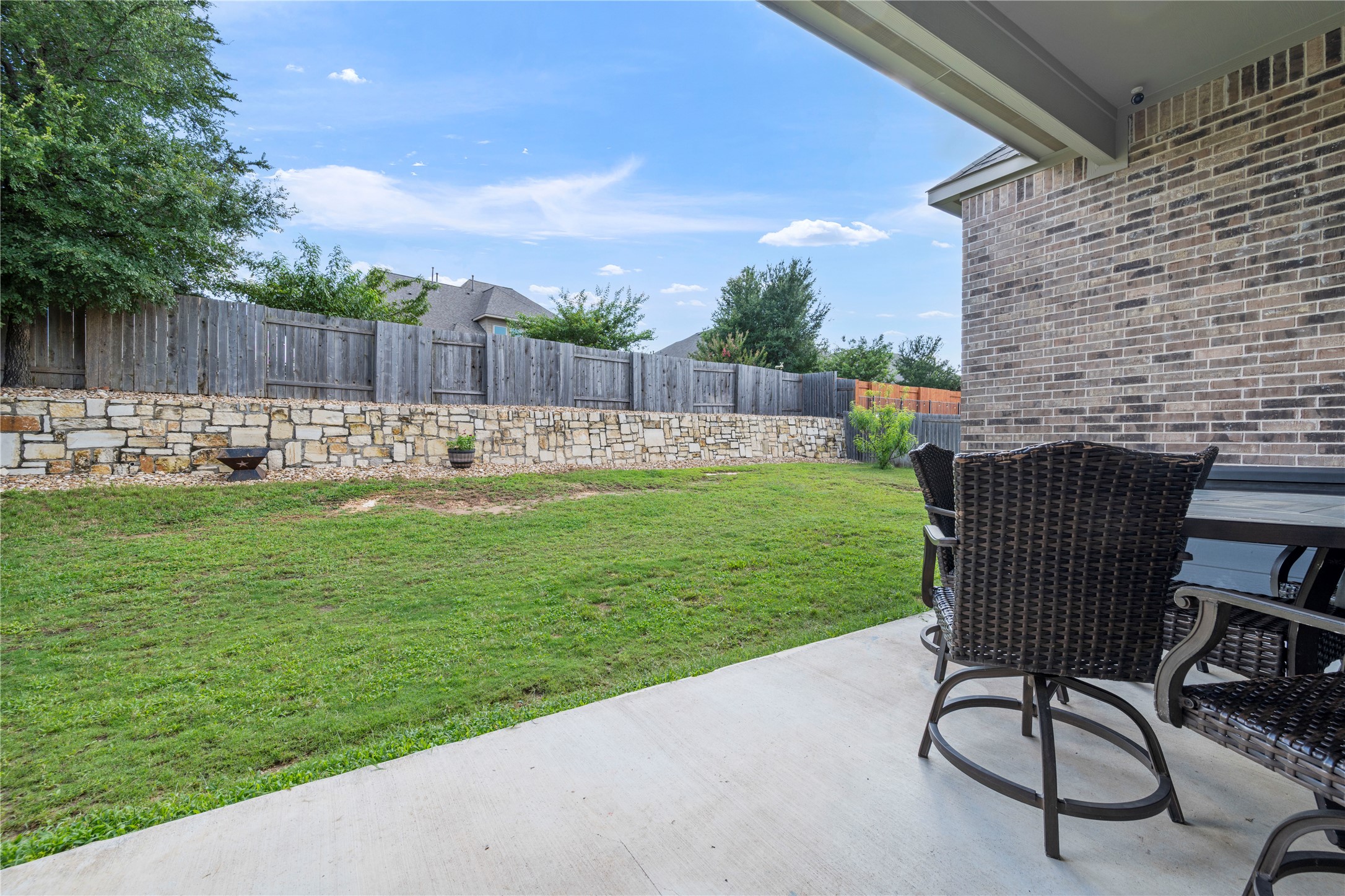 140 Catani Loop Georgetown, TX 78628 - Photo 36 of 36 A spacious backyard with a verdant lawn leads to a stone retaining wall and privacy fence.