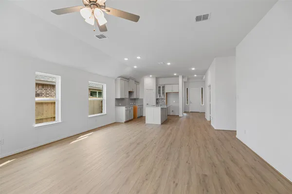 a view of an empty room with wooden floor and a ceiling fan