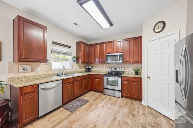 a kitchen with stainless steel appliances granite countertop a stove top oven a sink dishwasher a refrigerator and cabinets with wooden floor