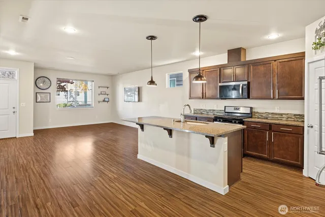 a kitchen with stainless steel appliances granite countertop a stove a sink dishwasher a refrigerator and a dining table with wooden floor