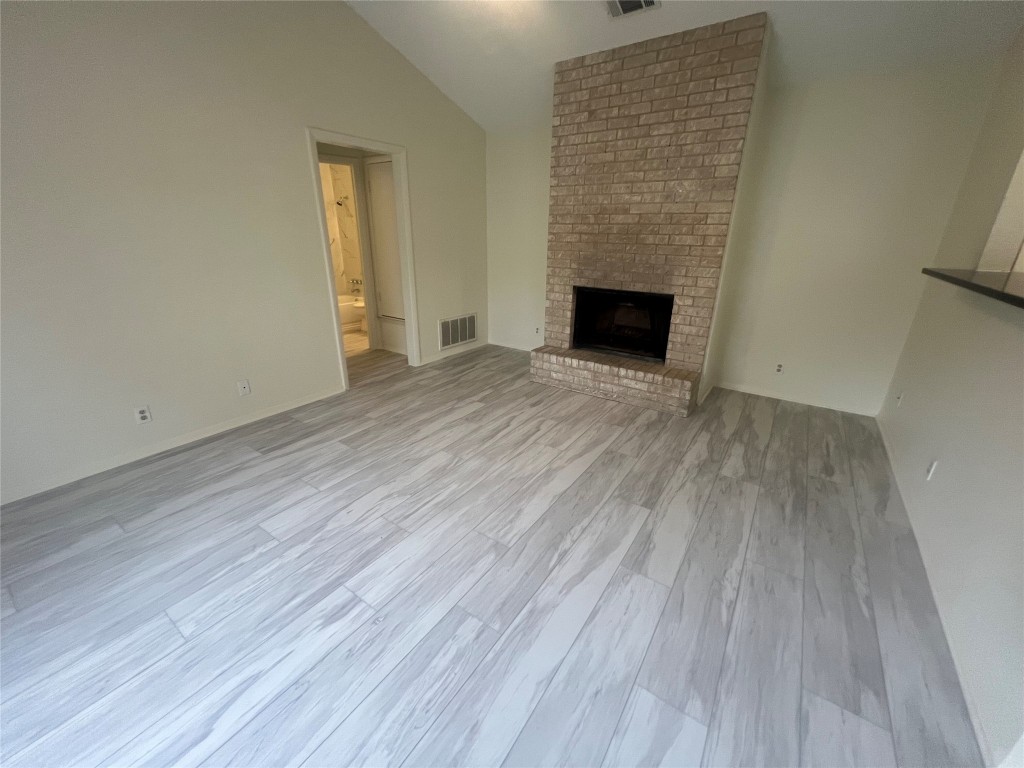 807 Lloyd Lane, Unit A Elgin, TX 78621 - Photo 6 of 16 Unfurnished living room with light wood-type flooring, a brick fireplace, and vaulted ceiling