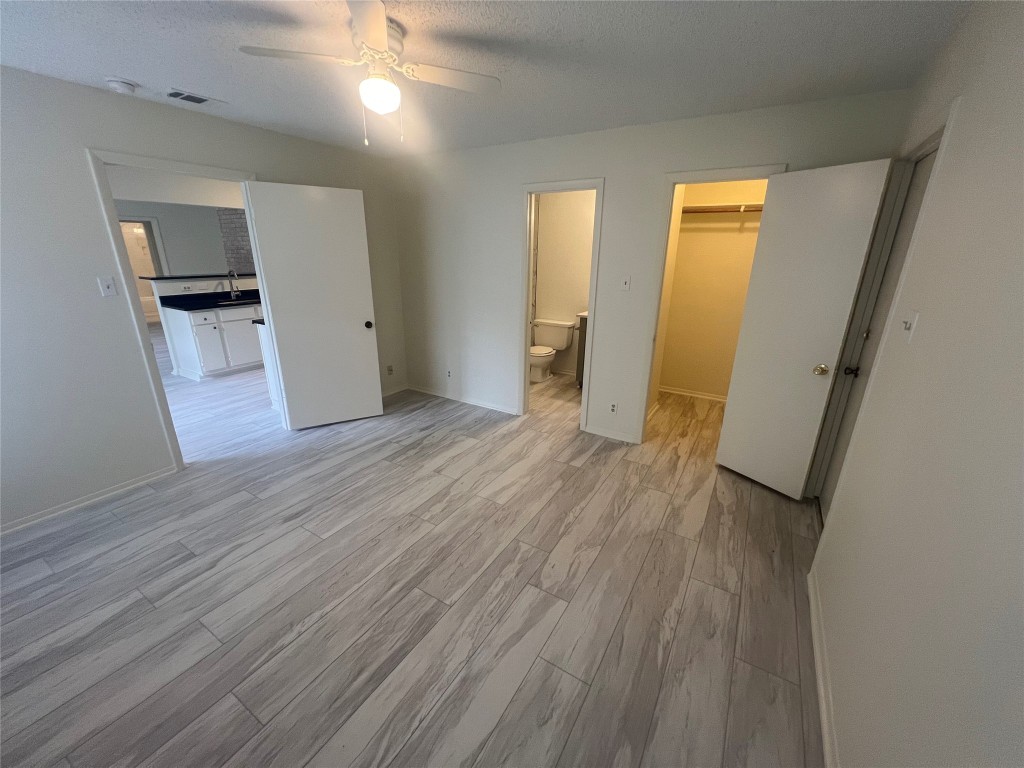 807 Lloyd Lane, Unit A Elgin, TX 78621 - Photo 8 of 16 Unfurnished bedroom with light wood-style flooring, a spacious closet, ceiling fan, a textured ceiling, and ensuite bathroom