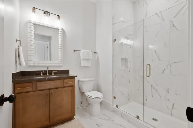 a bathroom with a granite countertop sink a toilet mirror and shower