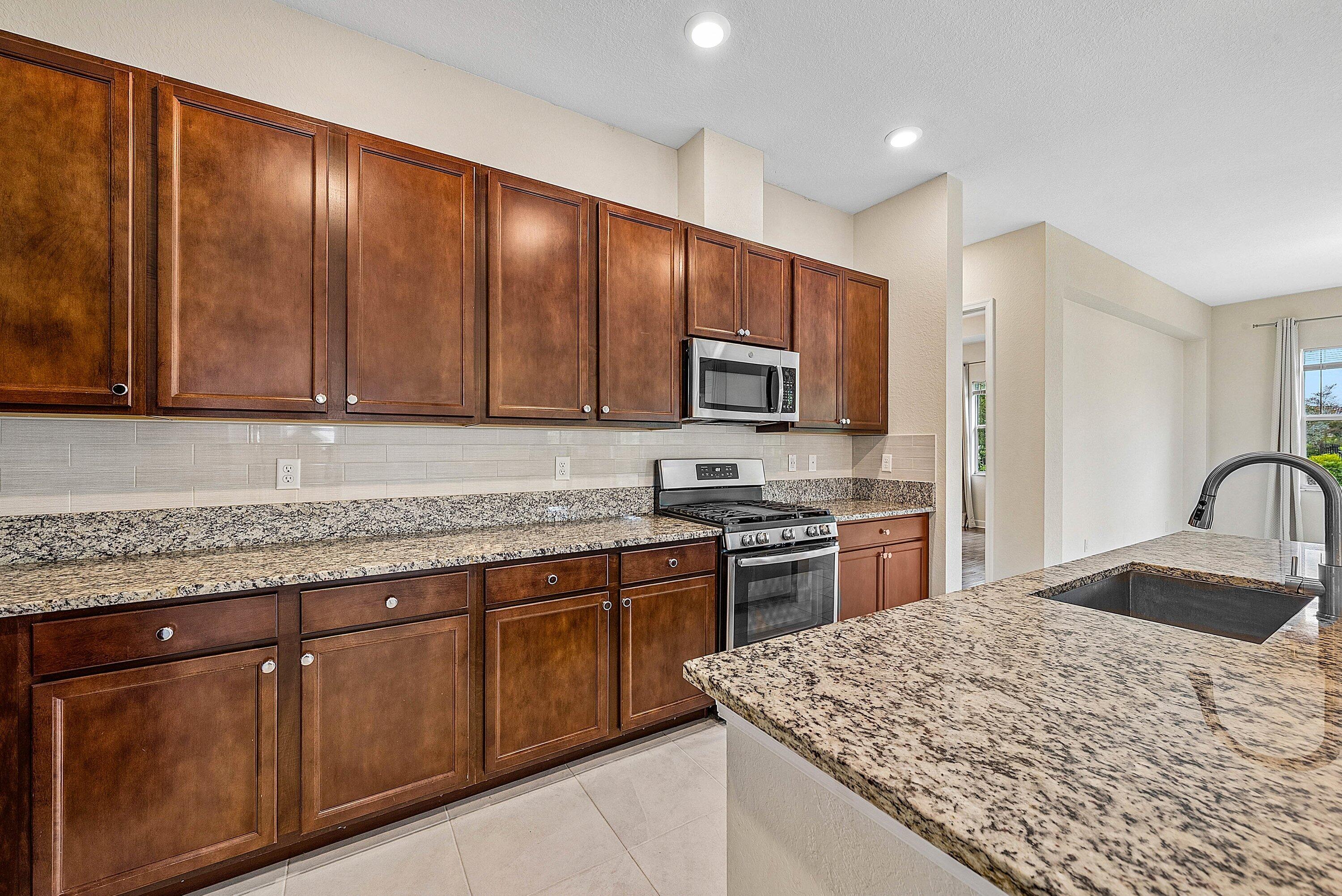 1031 Ember Ridge Run Loxahatchee, FL 33470 - Photo 26 of 52 a kitchen with stainless steel appliances granite countertop wooden cabinets a stove top oven a sink and dishwasher