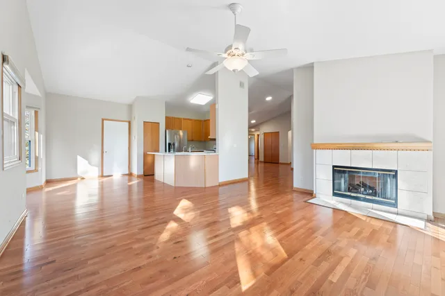 an empty room with wooden floor fireplace and kitchen view