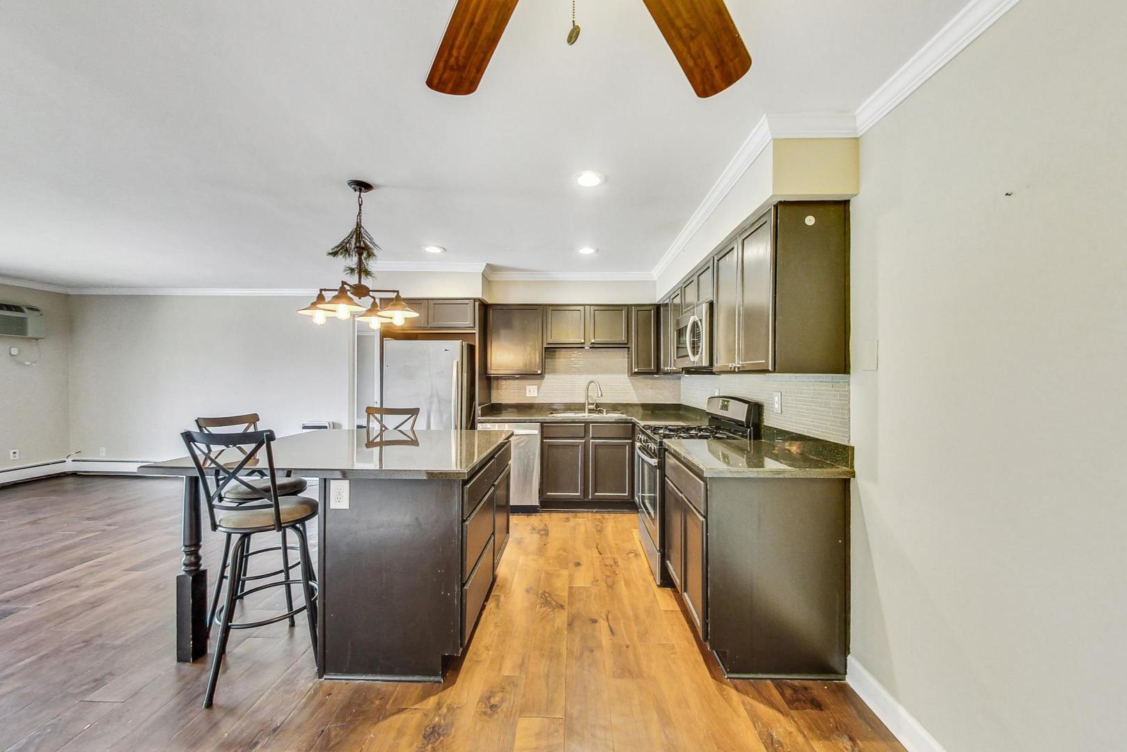 19398 Wolf Road, Unit 11 Mokena, IL 60448 - Photo 13 of 27 a kitchen with stainless steel appliances granite countertop a stove top oven a sink a dining table and chairs with wooden floor