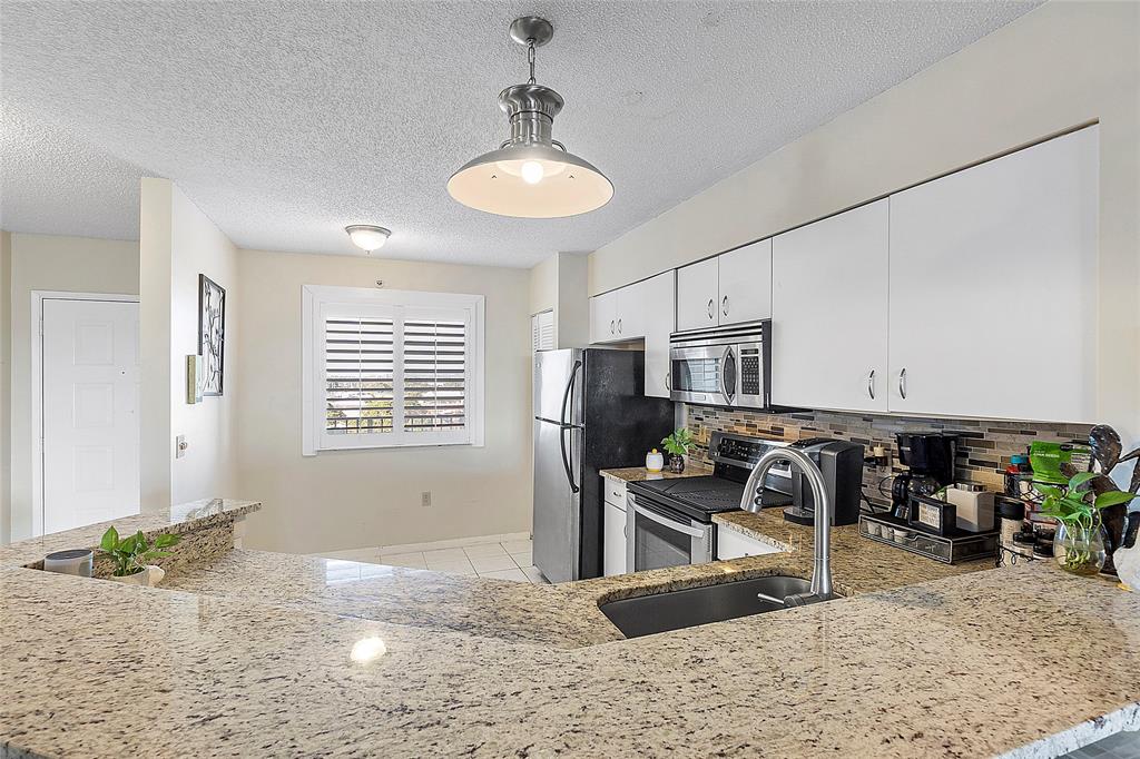 2240 North Cypress Bend Drive, Unit 908 Pompano Beach, FL 33069 - Photo 7 of 66 a view of a kitchen with kitchen island granite countertop a stove and a sink
