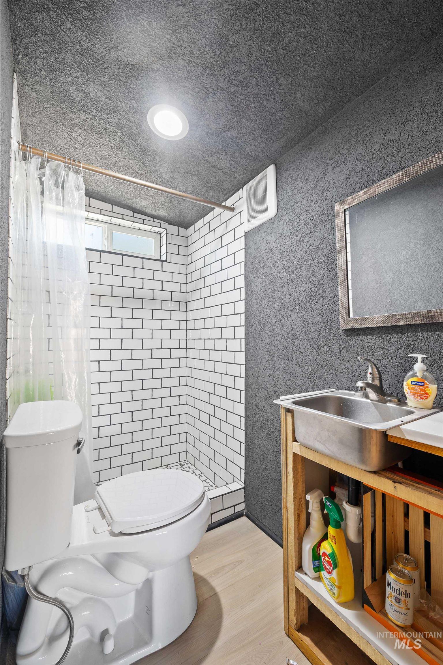 102 East 6th Street Rupert, ID 83350 - Photo 14 of 27 Compact bathroom featuring a subway tile shower enclosure, light wood-finish flooring, a contemporary toilet, a built-in sink vanity with open shelving, and recessed ceiling lighting