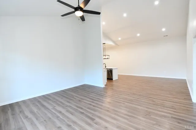 an empty room with wooden floor chandelier fan and windows