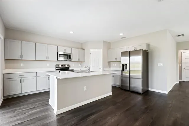 a kitchen with stainless steel appliances granite countertop a refrigerator a sink dishwasher a stove top oven a refrigerator and white cabinets with wooden floor