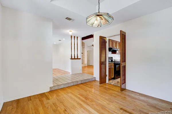 a view of an empty room with wooden floor and a kitchen