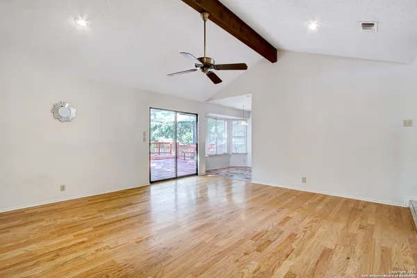 an empty room with wooden floor ceiling fan and windows