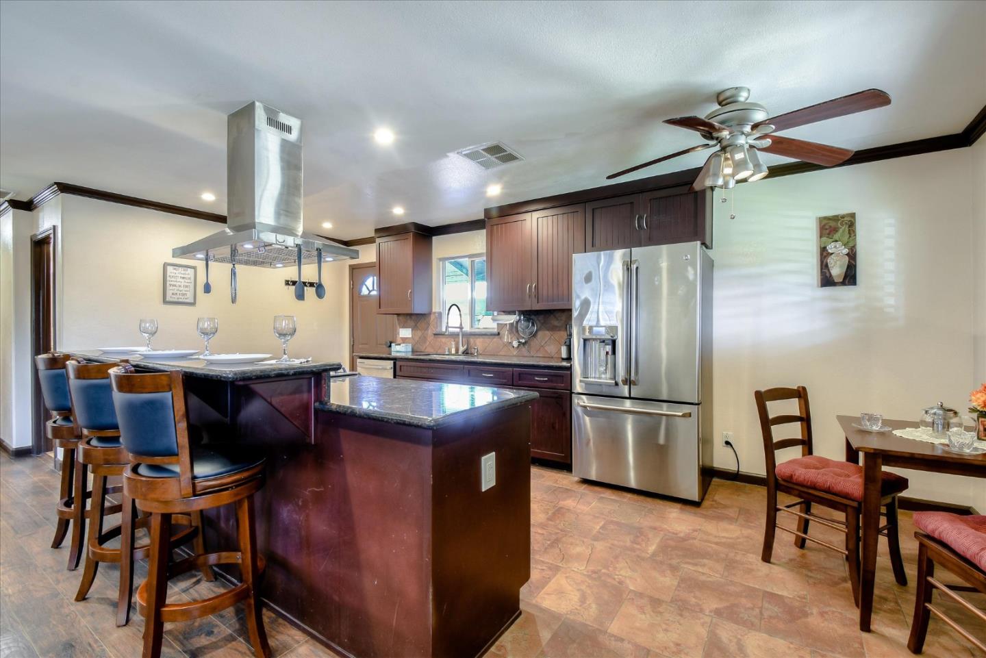 a kitchen with stainless steel appliances granite countertop a refrigerator a sink dishwasher a dining table and chairs with wooden floor