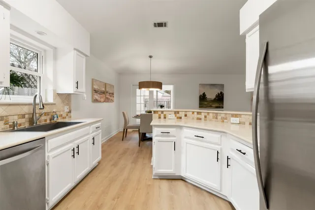 a large white kitchen with a stove a sink dishwasher and a refrigerator with wooden floor