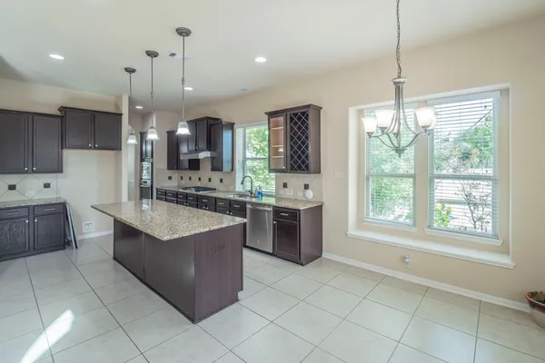 a large kitchen with kitchen island granite countertop a stove a sink a counter top space and cabinets