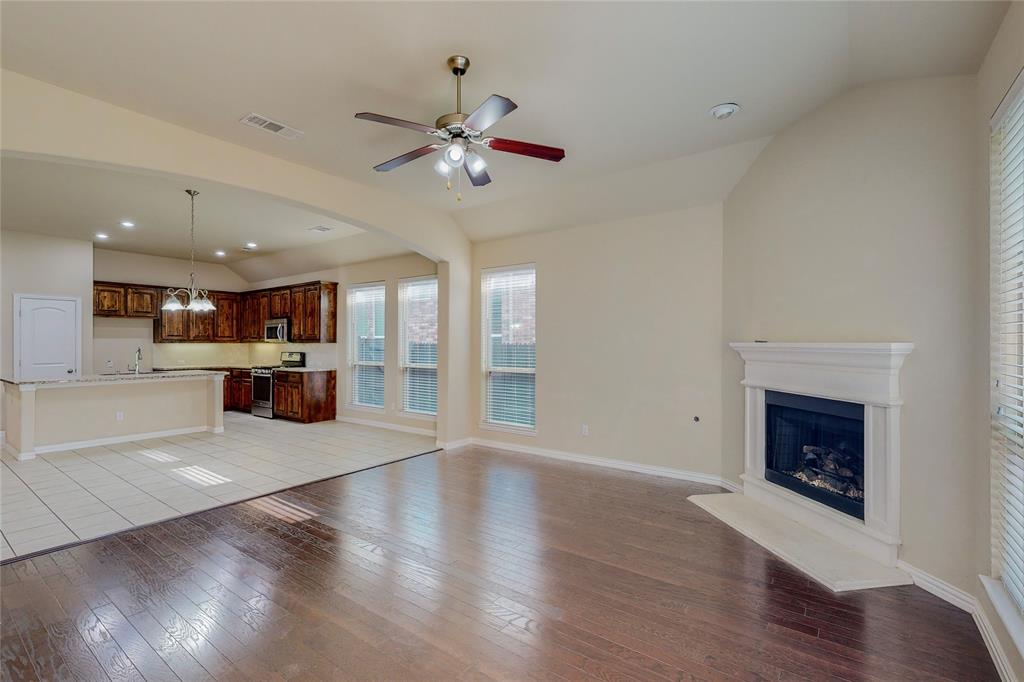 Unfurnished living room featuring lofted ceiling, light wood-type flooring, a fireplace with raised hearth, and ceiling fan with notable chandelier