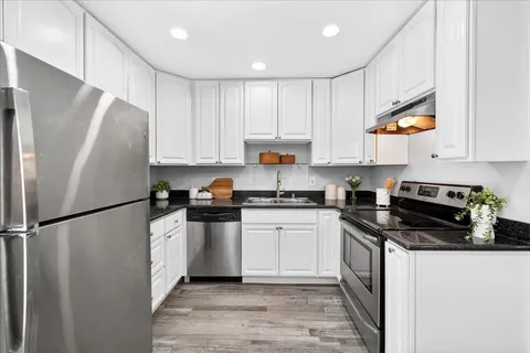 a kitchen with stainless steel appliances a refrigerator a sink and white cabinets