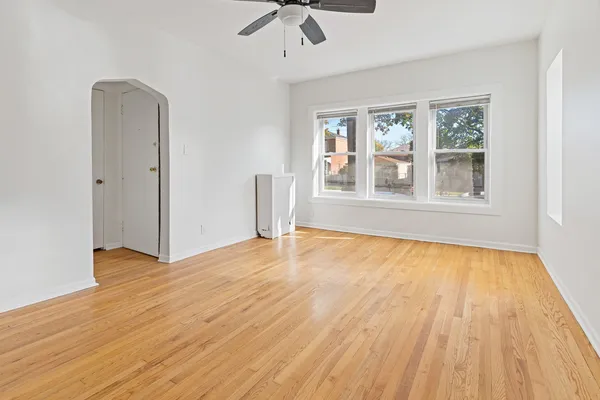 an empty room with wooden floor chandelier fan and windows