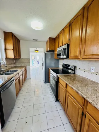 a kitchen with stainless steel appliances granite countertop a stove top oven a sink dishwasher and a refrigerator with wooden cabinets