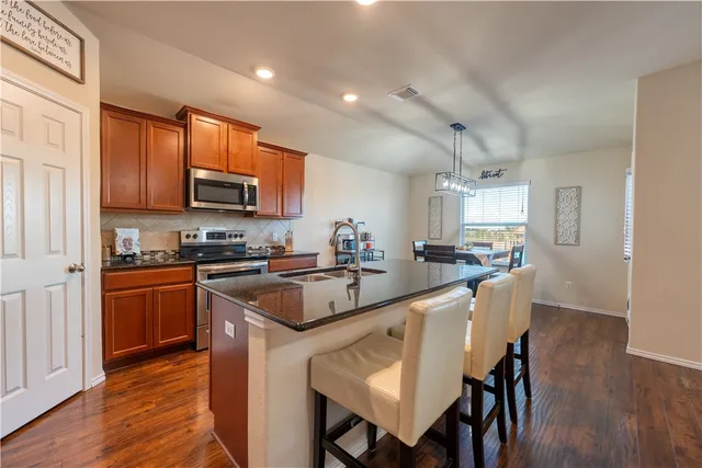 a kitchen with stainless steel appliances granite countertop a stove top oven a sink a refrigerator and a dining table with wooden floor