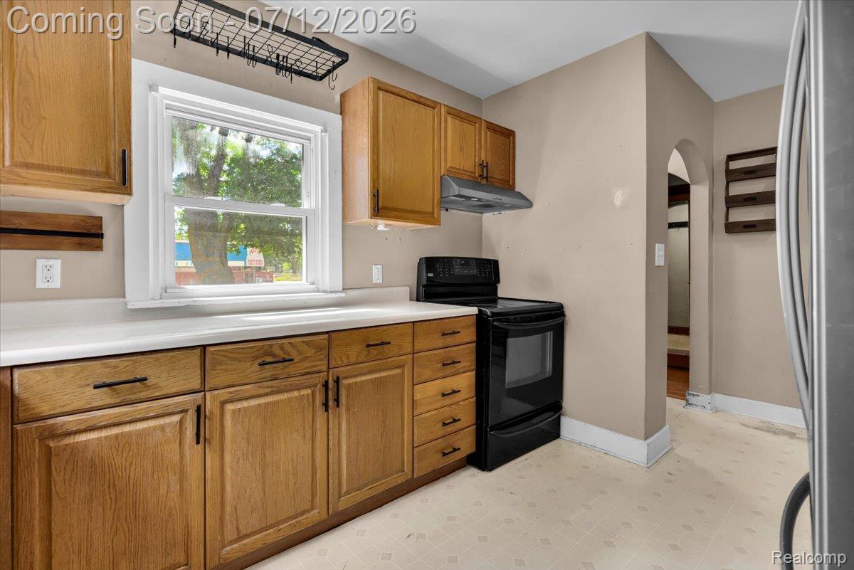 624 North Prospect Road Ypsilanti, MI 48198 - Photo 15 of 28 Kitchen featuring wood cabinetry, light-toned countertops, a black electric range with an overhead vent, and an arched doorway