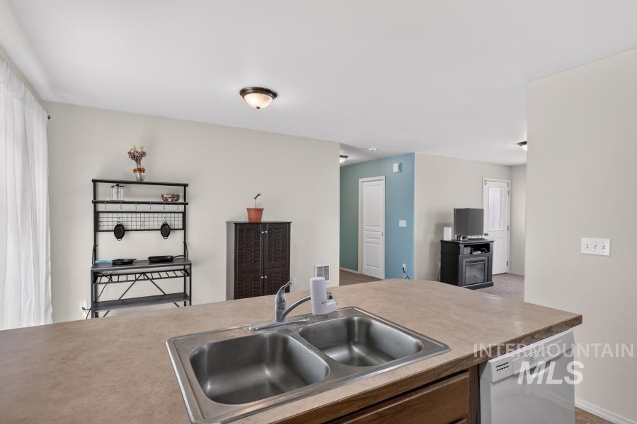1337 Bristol Road Moscow, ID 83843 - Photo 12 of 28 Kitchen island featuring a double basin stainless steel sink with a high-arc faucet, a light-toned countertop, and integrated dishwasher