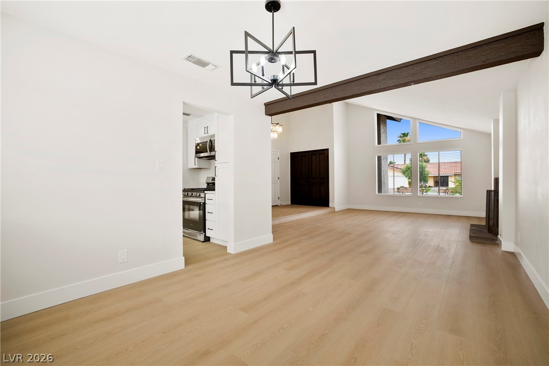 2411 Doherty Way Henderson, NV 89014 - Photo 6 of 34 A striking modern chandelier illuminates a spacious open-concept interior featuring light wood flooring and high vaulted ceilings.