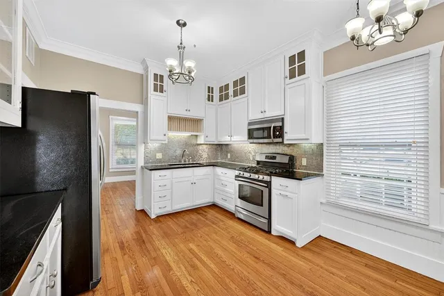 a large kitchen with stainless steel appliances granite countertop a stove a sink dishwasher a refrigerator white cabinets and wooden floor