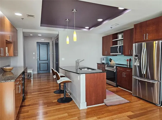 a kitchen with stainless steel appliances granite countertop a refrigerator a sink dishwasher a stove and a microwave oven on dining table with wooden floor