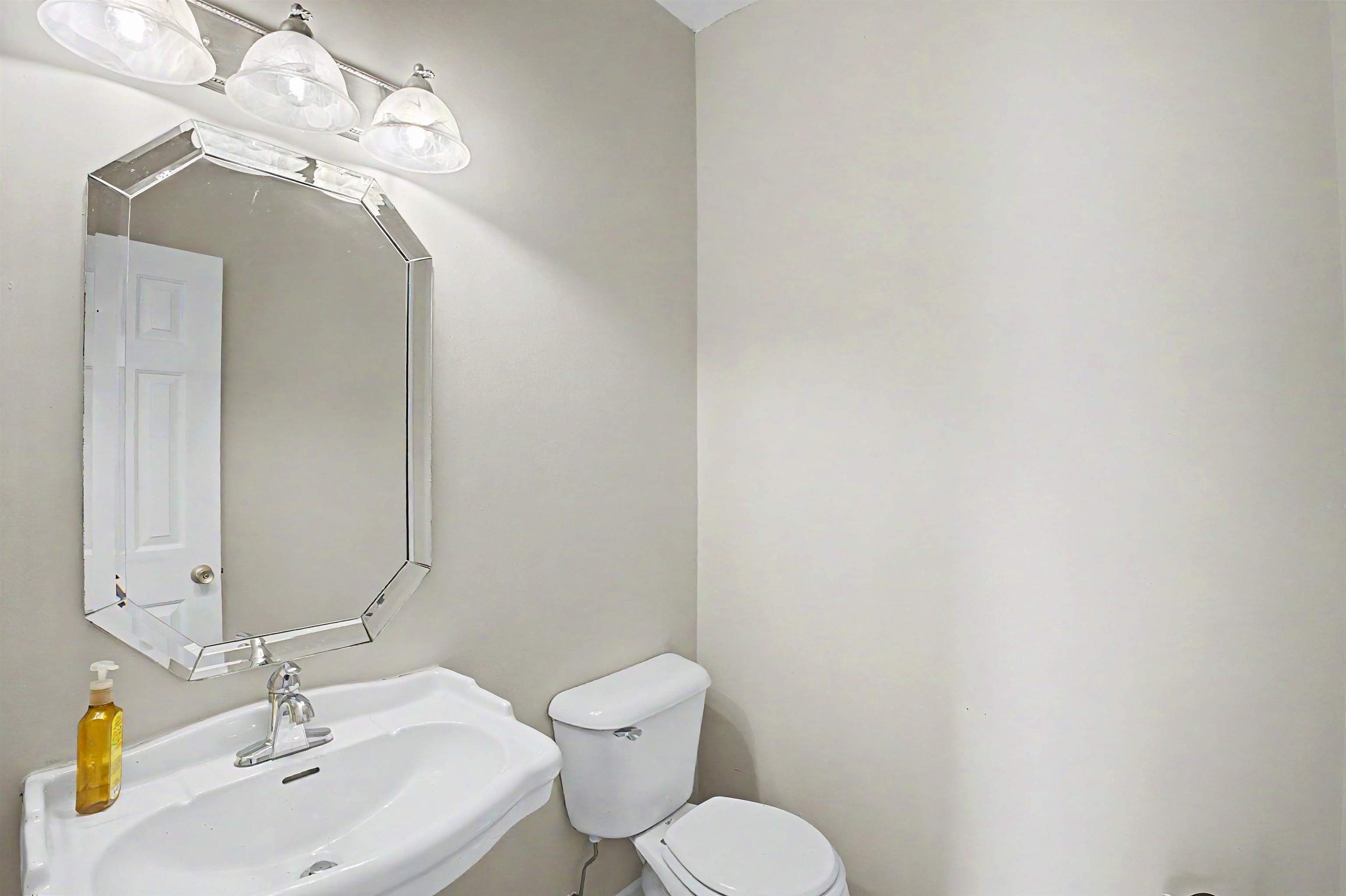 134 Rembert Drive Atoka, TN 38004 - Photo 35 of 38 Bathroom featuring a white pedestal sink with a chrome faucet, an octagonal frameless mirror, and a three-light vanity fixture