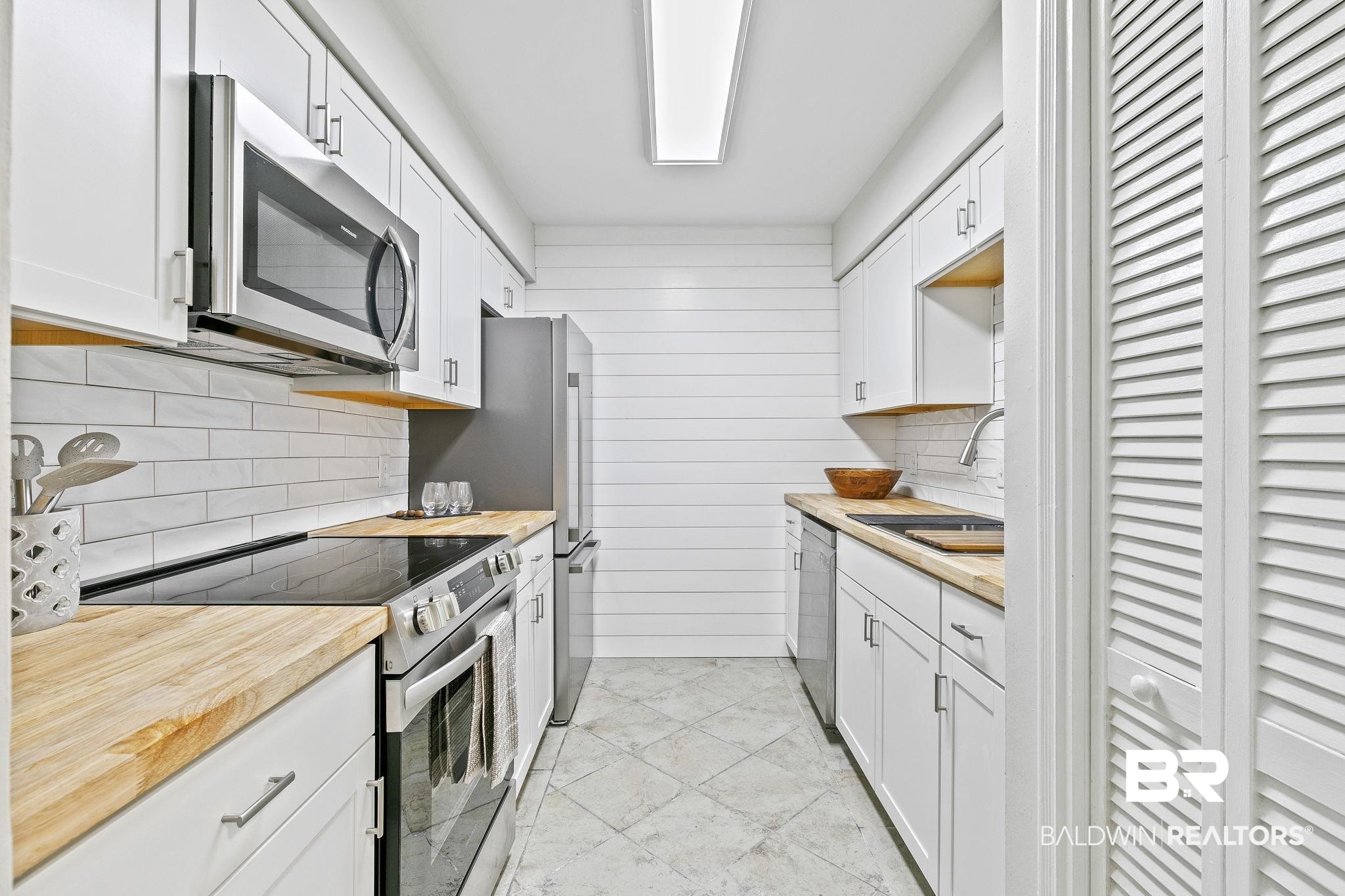 110 5th Street, Unit C103 Daphne, AL 36526 - Photo 17 of 46 Kitchen with sink, wooden walls, backsplash, white cabinets, and appliances with stainless steel finishes
