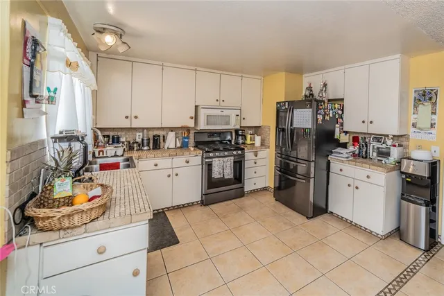 a kitchen with granite countertop a refrigerator sink stove and white cabinets