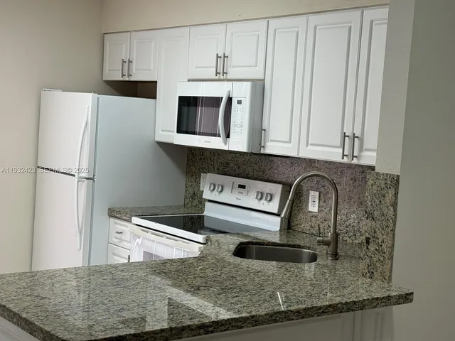 a kitchen with stainless steel appliances granite countertop a sink a microwave a refrigerator and white cabinets