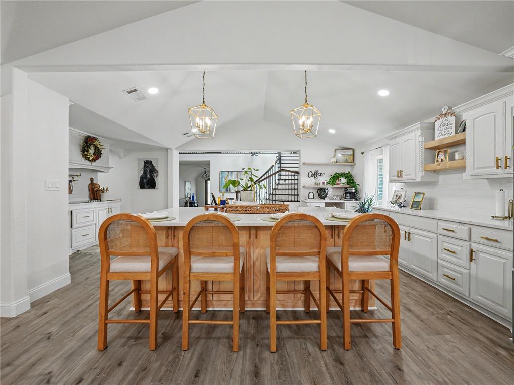 6701 Nauert Road Forest Hill, TX 76140 - Photo 9 of 40 Kitchen featuring a central island with countertop seating, white cabinetry with gold-tone hardware, subway tile backsplash, wood-finish flooring, and vaulted ceiling with pendant lighting