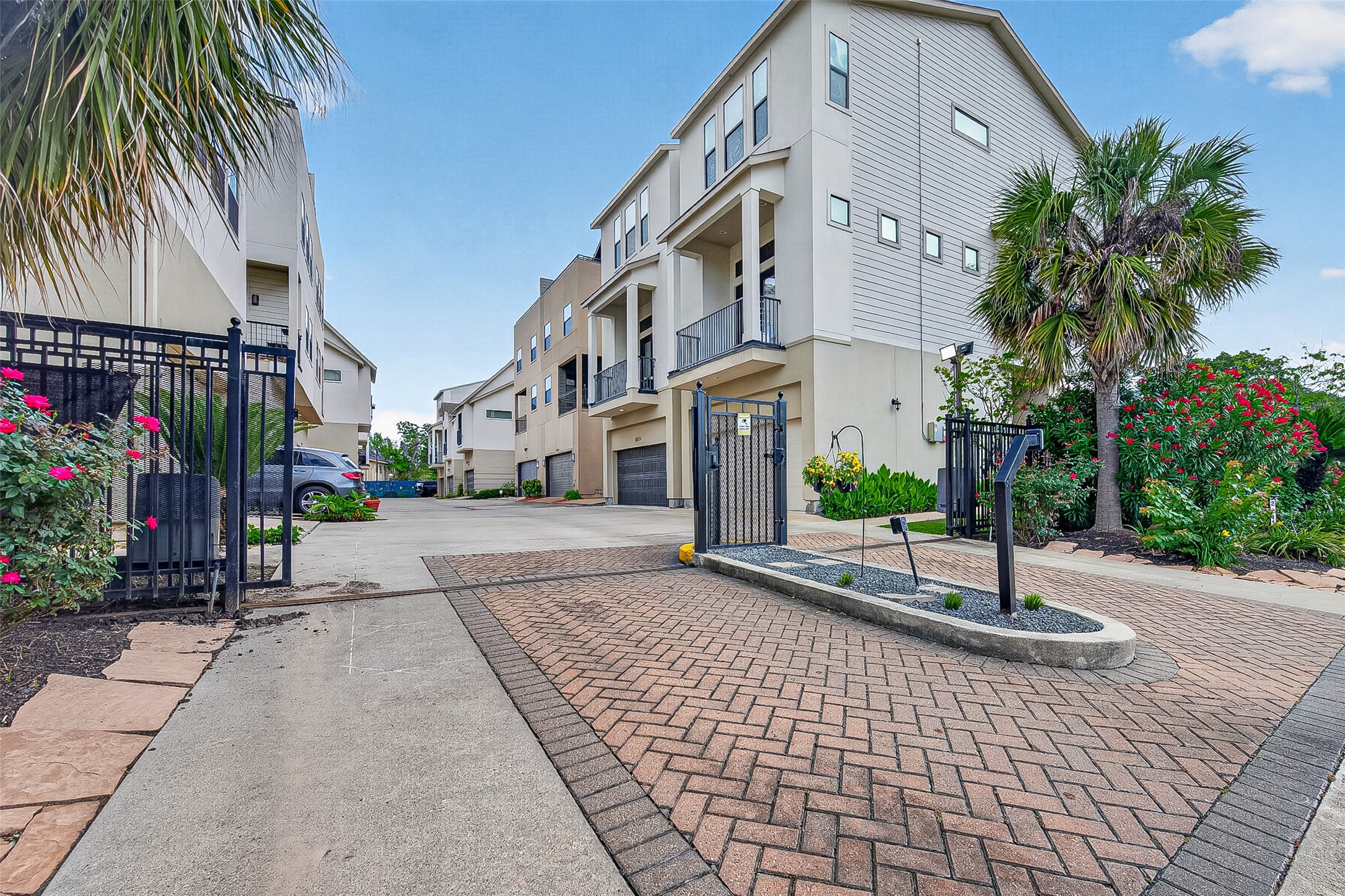 2611 Riverside Drive, Unit C Houston, TX 77004 - Photo 1 of 50 Modern four-story townhouse with a private driveway and gated entry. The exterior features a clean, contemporary design with large windows and a two balconies. The gated community has beautiful landscaped surrounded by palm trees and flowers, creating an inviting atmosphere.