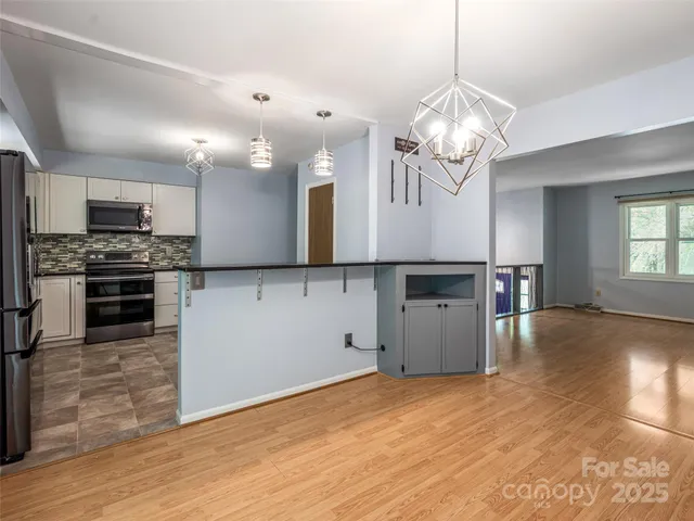 a kitchen with stainless steel appliances granite countertop a refrigerator a sink dishwasher a stove and a dining table with wooden floor