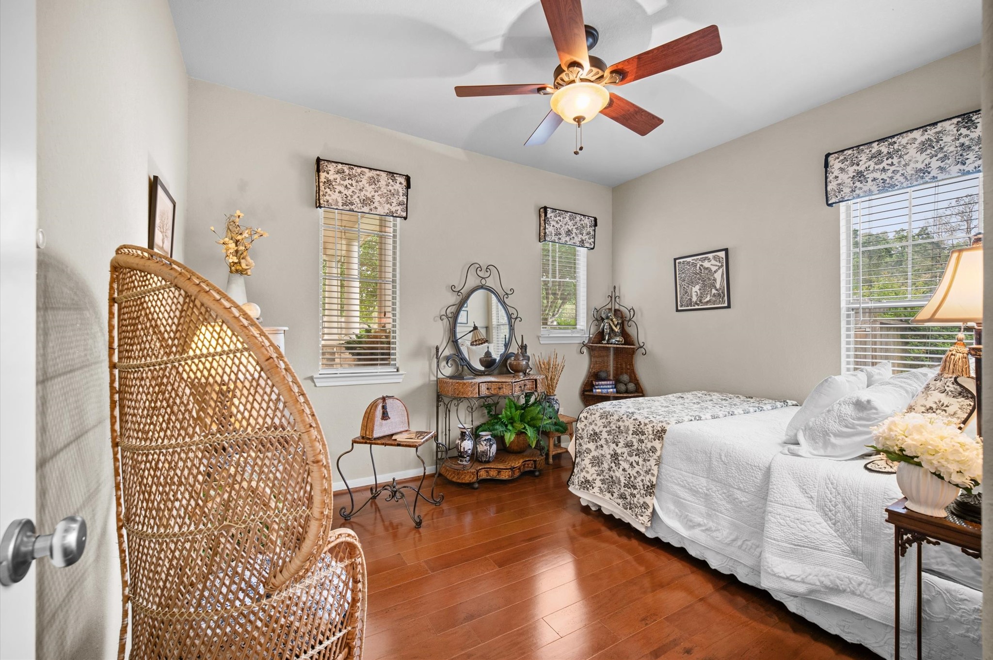 1603 Claytons Bend Court Spring, TX 77386 - Photo 11 of 38 This cozy bedroom features warm wood flooring, a ceiling fan, and ample natural light from three windows. It includes a comfortable bed, decorative accents, and a charming wicker chair, creating a welcoming and serene atmosphere.