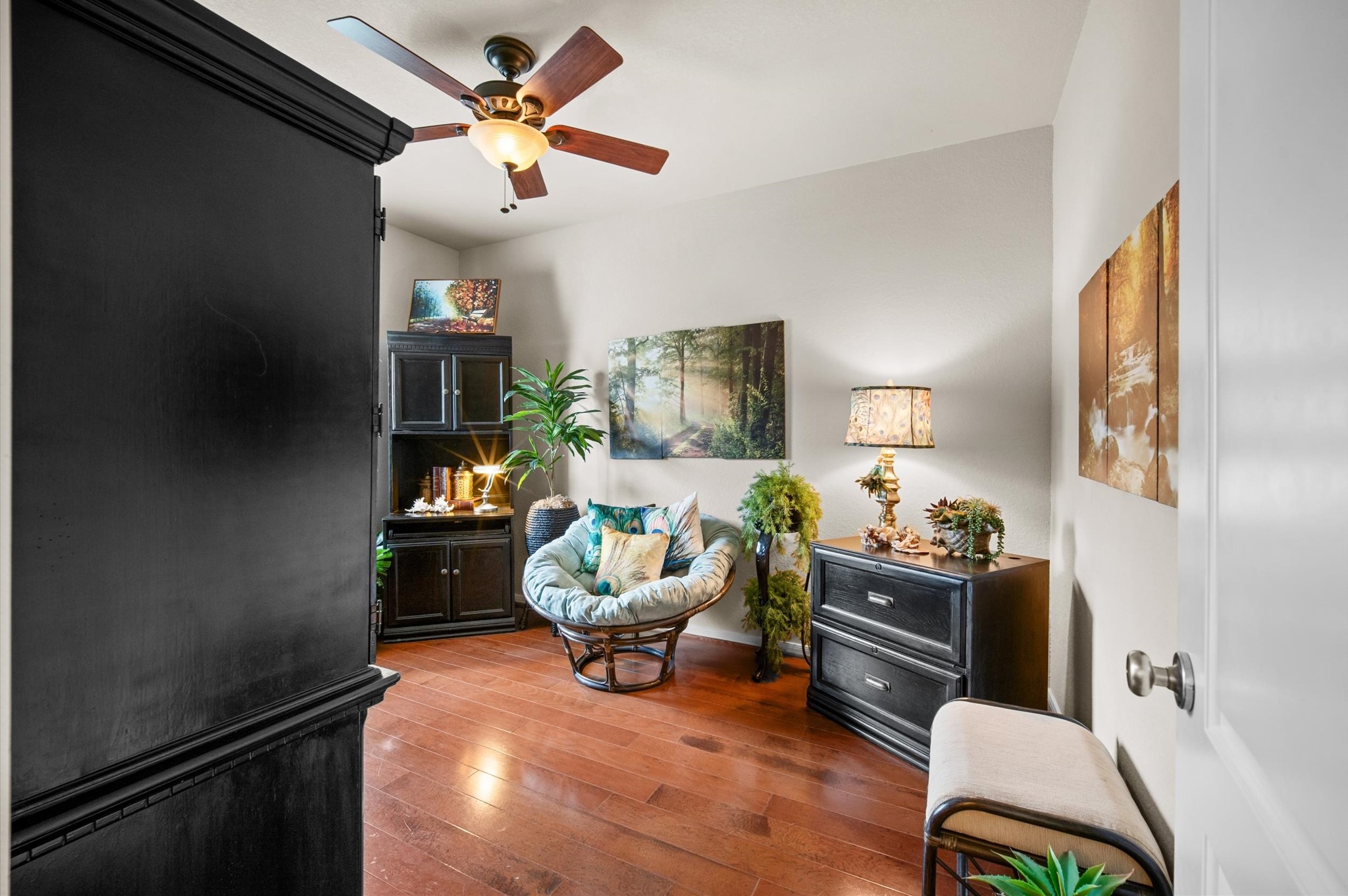 1603 Claytons Bend Court Spring, TX 77386 - Photo 13 of 38 This cozy room features hardwood floors and a warm, inviting atmosphere. It includes a ceiling fan, comfortable seating, and stylish dark wood furniture, perfect for relaxation or reading. The decor is complemented by plants and nature-themed artwork, creating a serene ambiance.