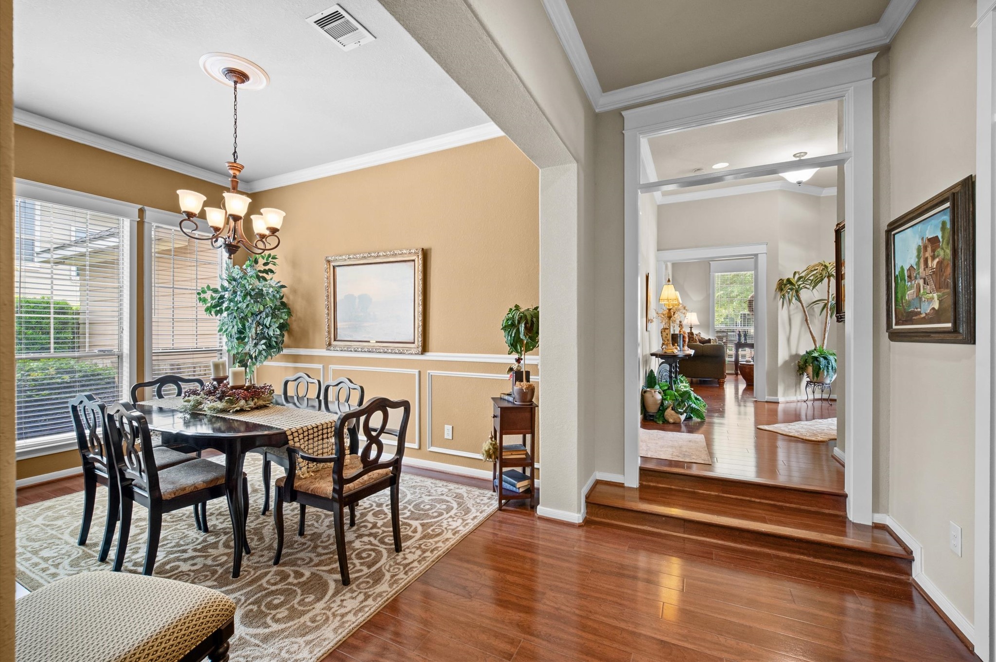 1603 Claytons Bend Court Spring, TX 77386 - Photo 15 of 38 This photo showcases a warm, inviting dining area with a large window for natural light, elegant chandelier, and detailed molding. The adjoining hallway leads to a cozy living space with hardwood floors and tasteful decor, highlighting a seamless flow between rooms.