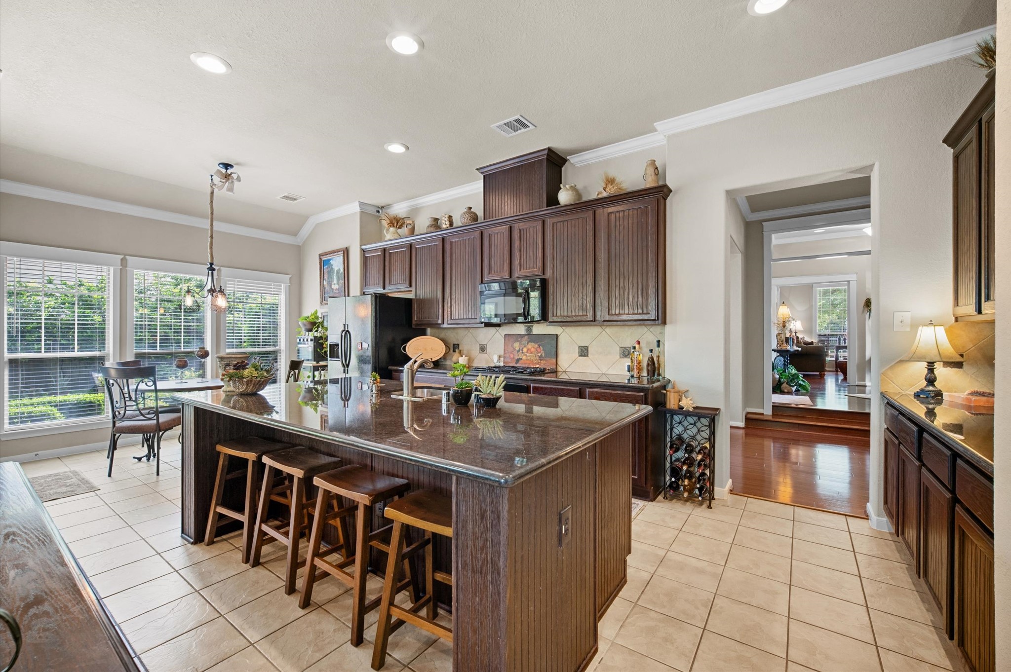 1603 Claytons Bend Court Spring, TX 77386 - Photo 16 of 38 Spacious kitchen with a large island and bar seating, featuring dark wood cabinetry and modern appliances. It has ample natural light from large windows and an adjacent dining area with garden views.