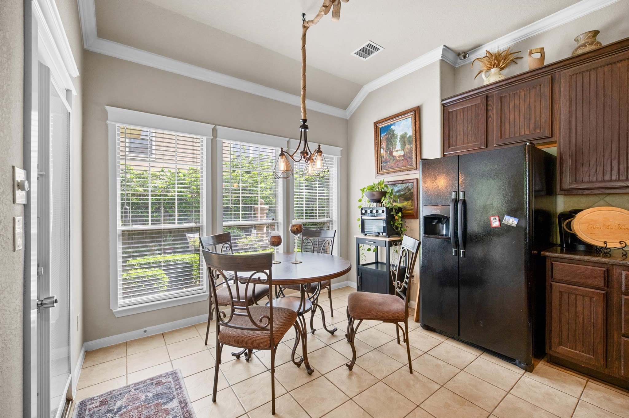 1603 Claytons Bend Court Spring, TX 77386 - Photo 17 of 38 This is a cozy kitchen dining area featuring a round table with four chairs, large windows for natural light, and a black refrigerator. The space has tiled floors, dark wood cabinets, and a light fixture overhead, offering a welcoming atmosphere for meals.