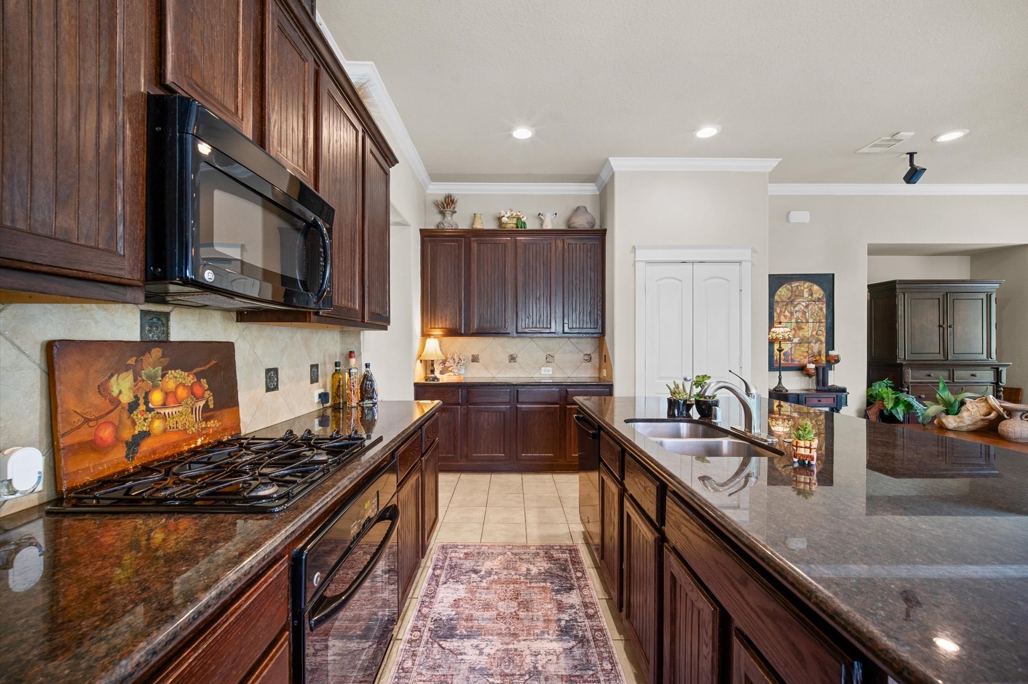 1603 Claytons Bend Court Spring, TX 77386 - Photo 18 of 38 This kitchen features rich dark wood cabinetry and sleek granite countertops, providing ample space for cooking and entertaining. The modern appliances, including a built-in microwave and stovetop, complement the elegant design. A spacious island with a sink adds functionality, while decorative elements give the space a welcoming touch.