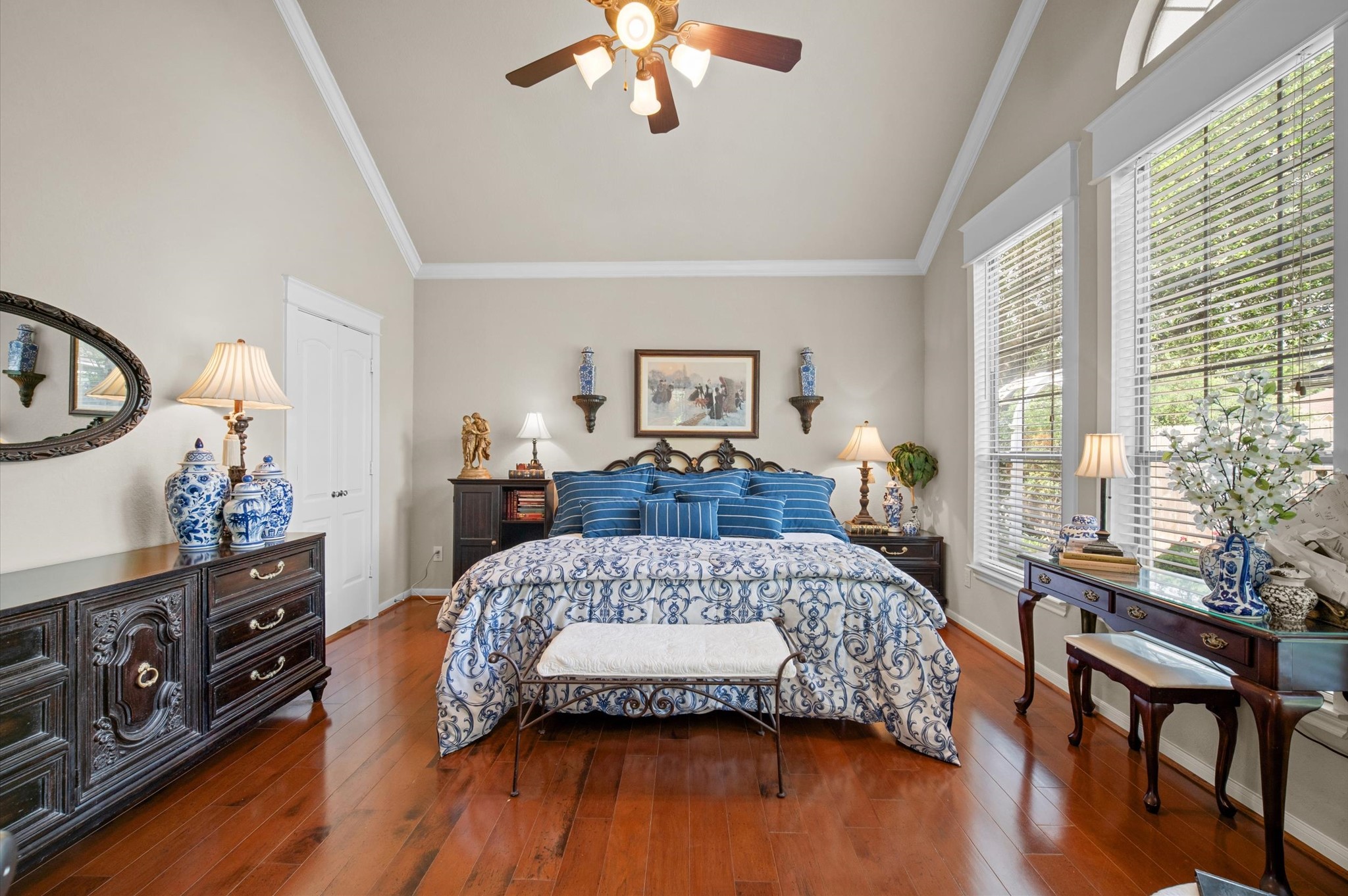 1603 Claytons Bend Court Spring, TX 77386 - Photo 24 of 38 This elegant bedroom features a high ceiling with a ceiling fan, hardwood floors, and large windows providing ample natural light. The room is tastefully decorated with classic furniture, including a comfortable bed with blue and white bedding, matching lamps, and decorative vases.