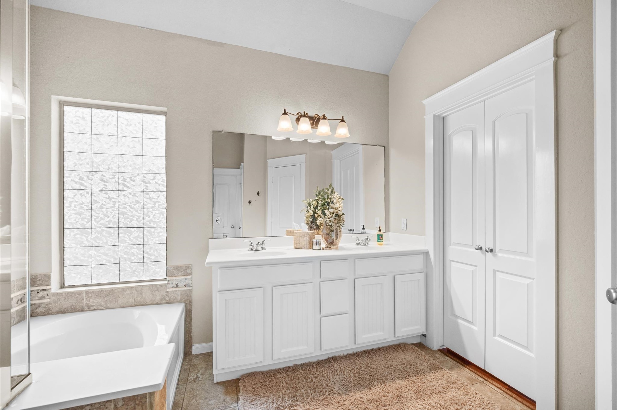 1603 Claytons Bend Court Spring, TX 77386 - Photo 27 of 38 This bathroom features a spacious vanity with dual sinks, a large mirror, and elegant lighting. It includes a cozy bathtub adjacent to a textured glass window, providing natural light while maintaining privacy. The neutral tones and ample storage offer a clean, inviting space.