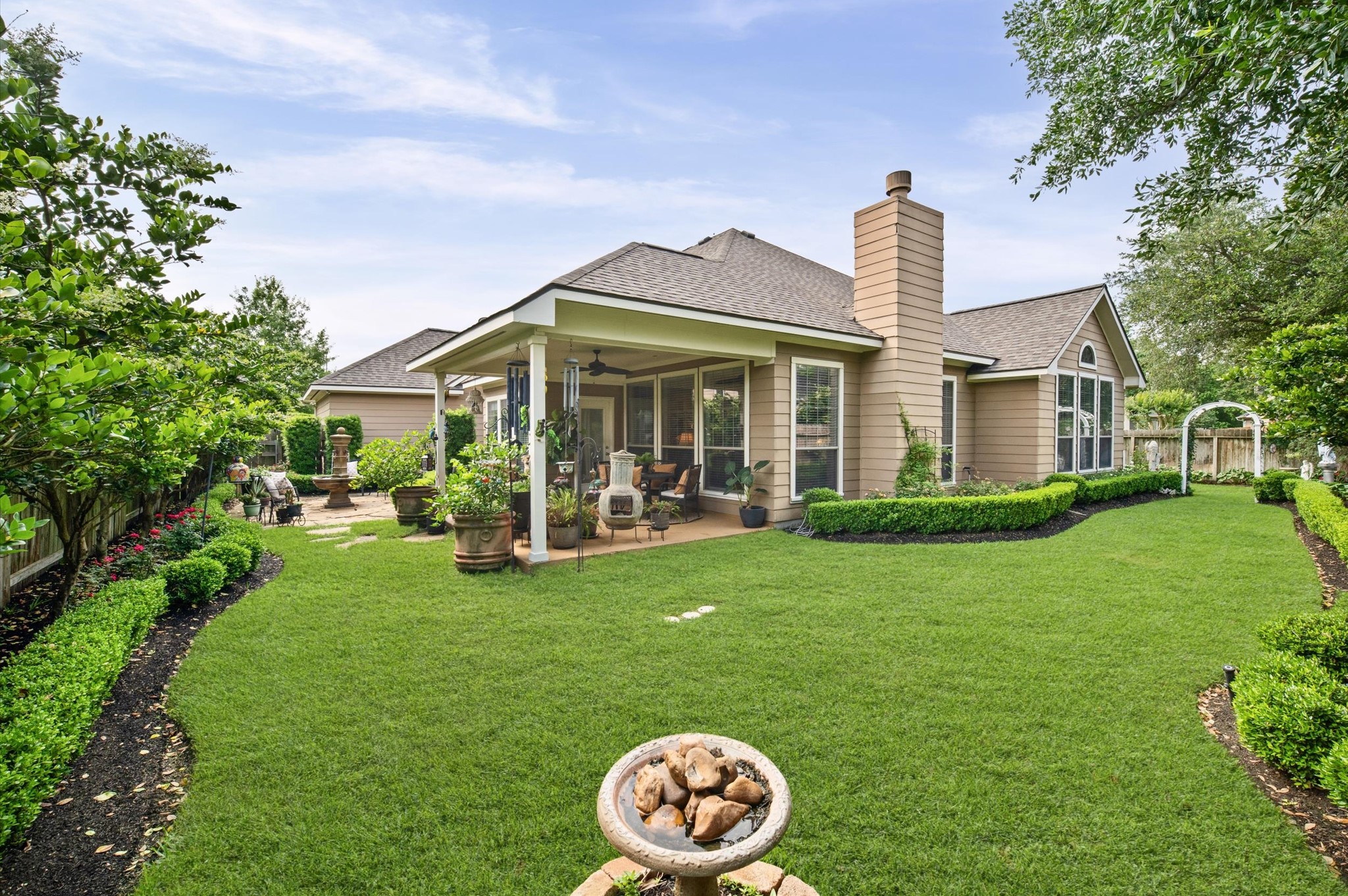 1603 Claytons Bend Court Spring, TX 77386 - Photo 28 of 38 This photo showcases a charming home with a well-maintained backyard featuring lush green lawn, manicured hedges, and a cozy covered patio. Perfect for outdoor relaxation and entertaining.
